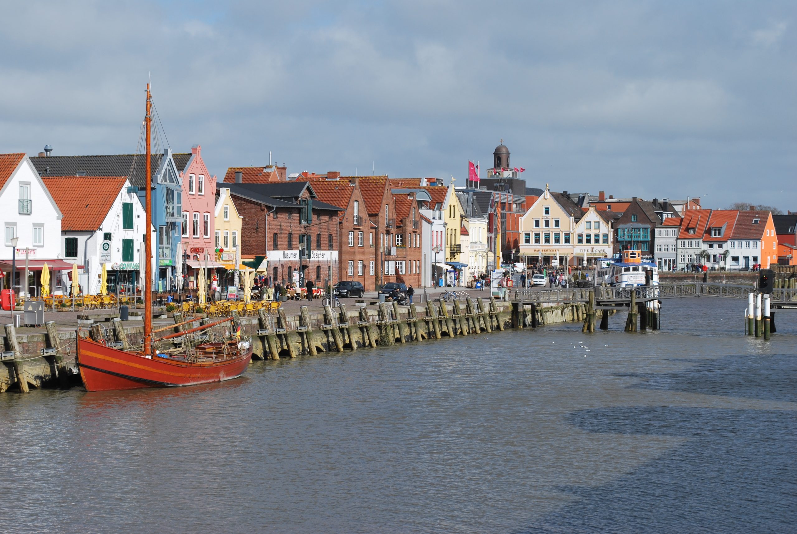 Der Husumer Hafen mit historischen Gebäuden, Promenade und kleinen Segelbooten.